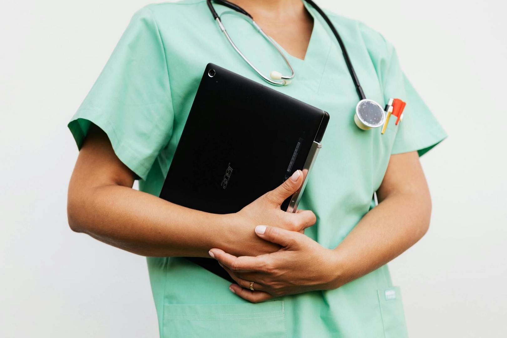 Osoba w zielonym uniformie medycznym trzyma tablet, z stetoskopem zawieszonym na szyi.